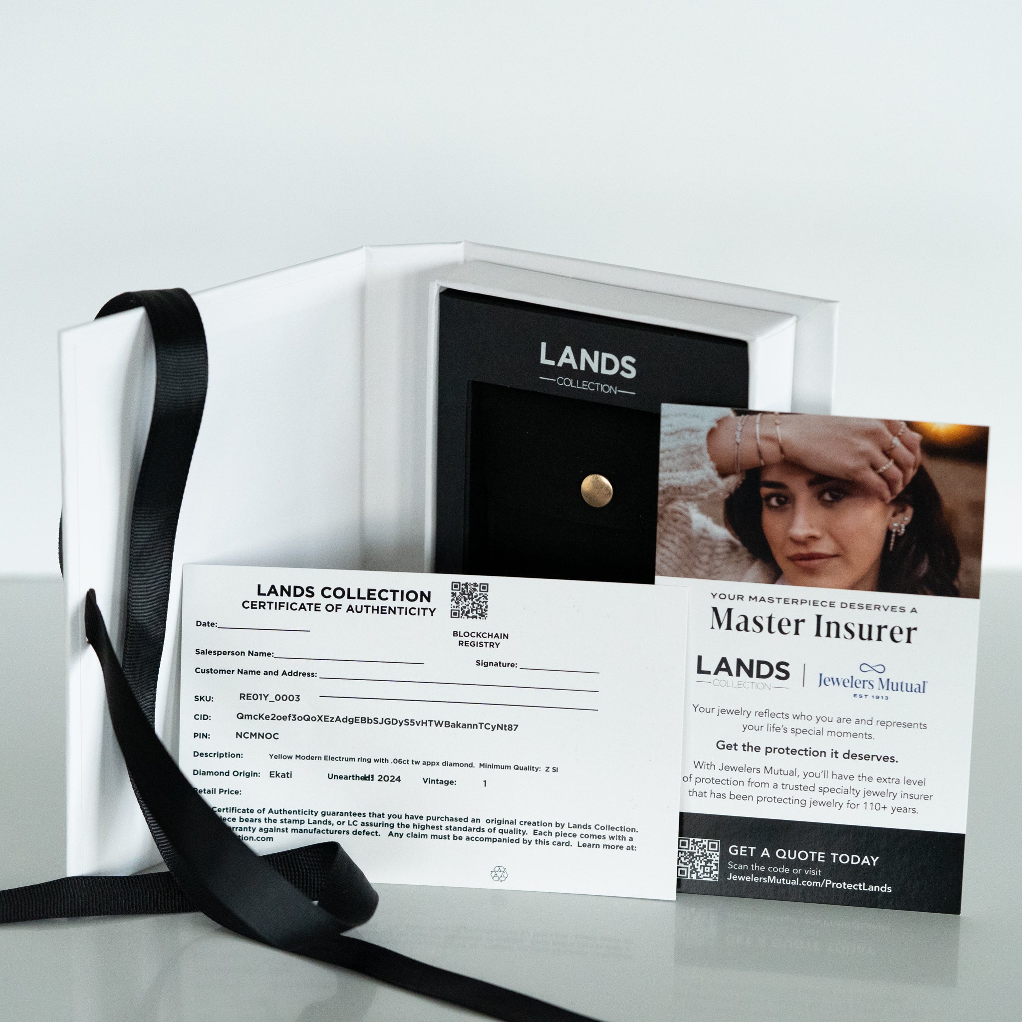 White 7 x 5 x 1 inch branded gift box with black silk ribbon on white background open to display certificate of authenticity, blockchain registry and insurance card