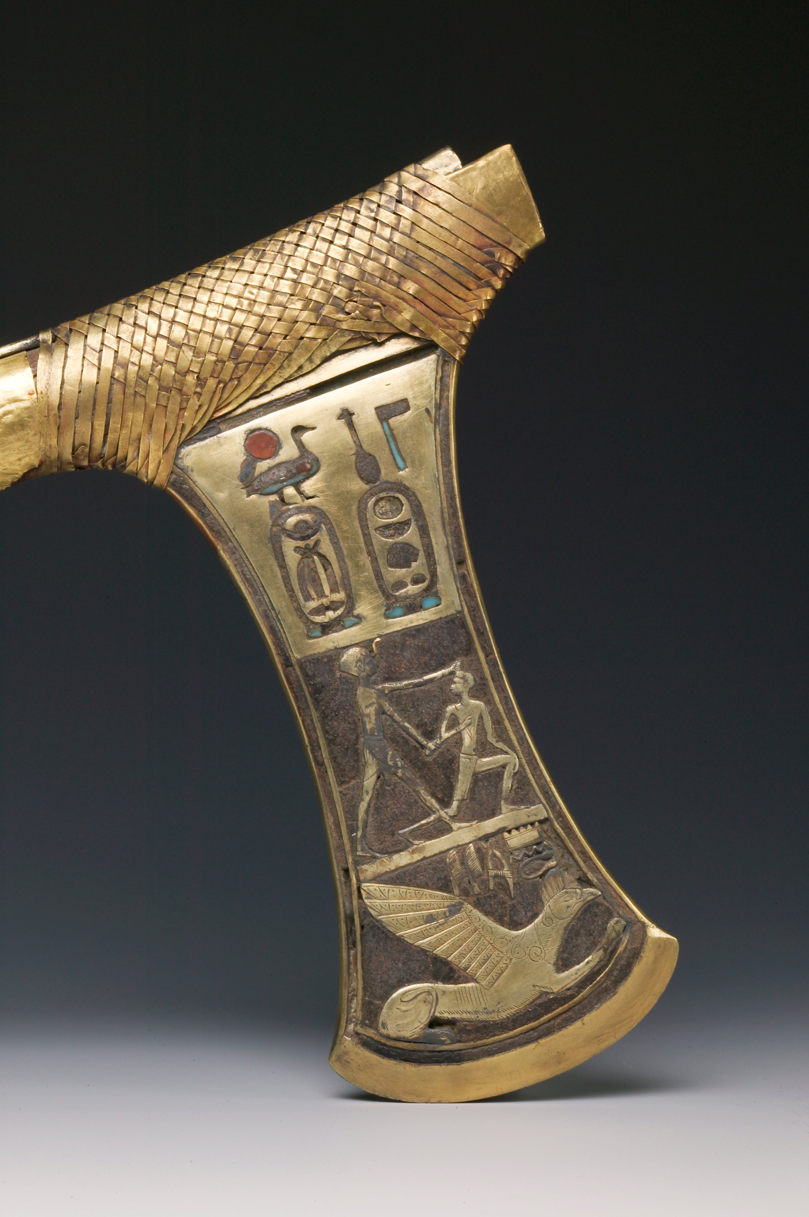It is admired for the gilded cedar wood handle and its copper blade. One of the sides of the blade is adorned with some scenes for Heh, Nekhbet, and other deities who are supposed to protect the pharaoh. The other side of the plade depicts the pharaoh tormenting one of his enemies as a symbol for sovereign power , topped with some cartouches with the names and titles of Ahmes. This gold ceremonial axe was discovered among the treasures in the Tomb of Ahmes in Dra Abu El Naga. Gold and wood.